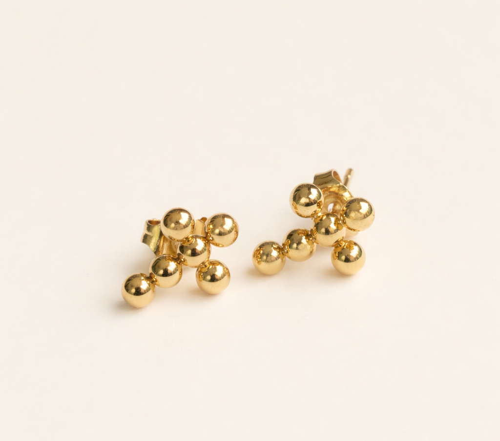 Gold beaded cross earrings on a beige background