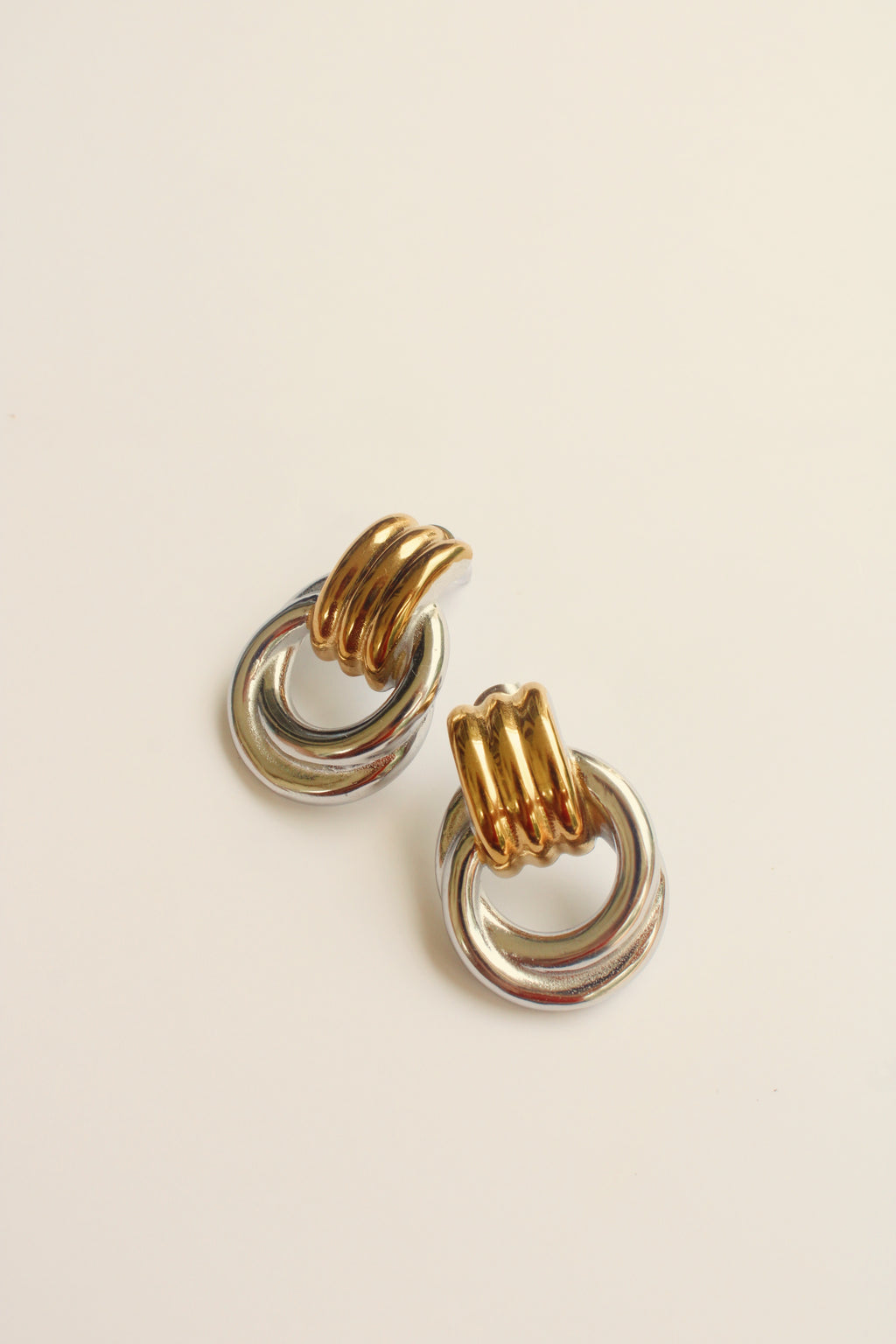 Pair of gold and silver vintage style hoop earrings on a beige background