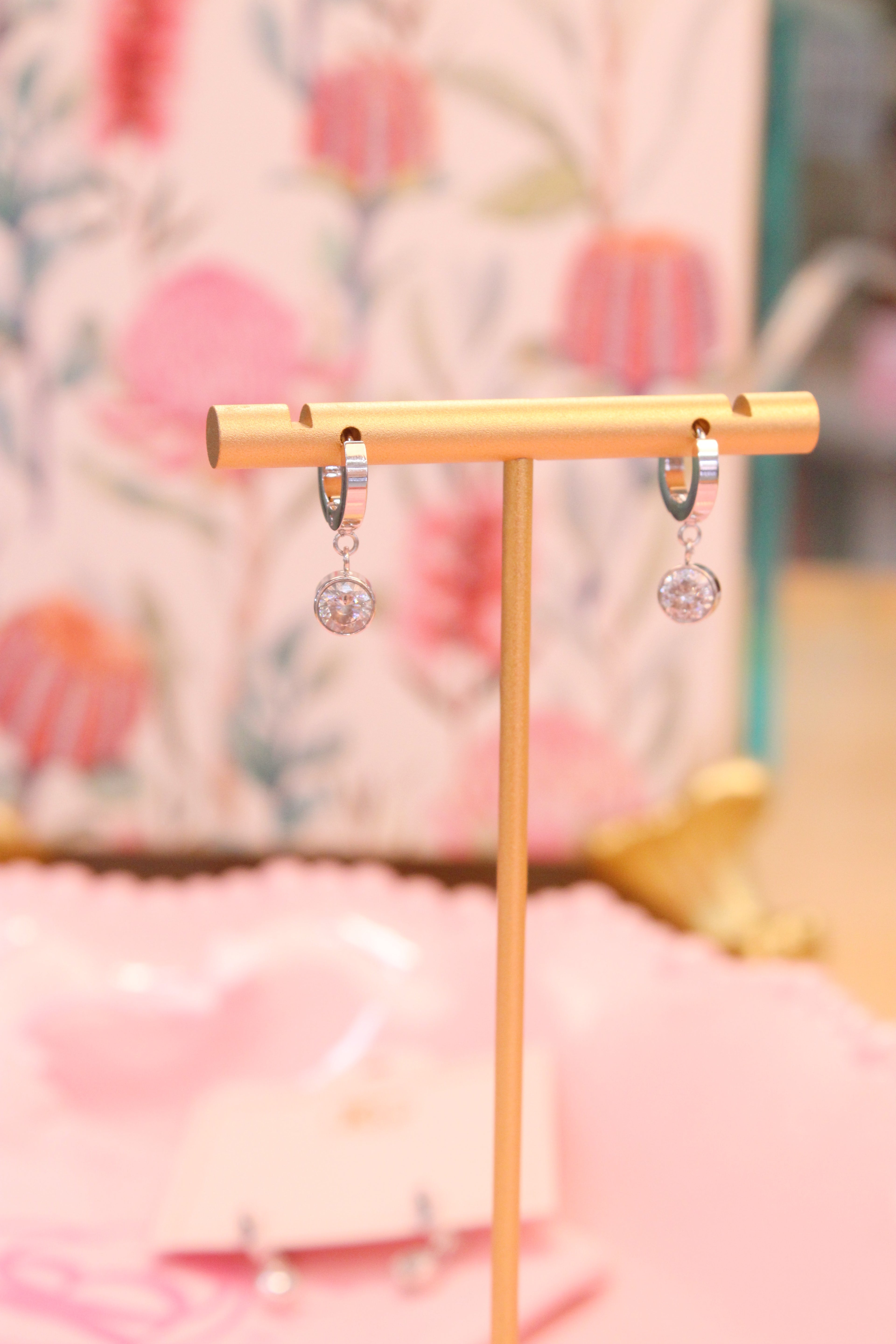 Gold earring stand with Silver hoops with drop diamond on a blurred floral backdrop
