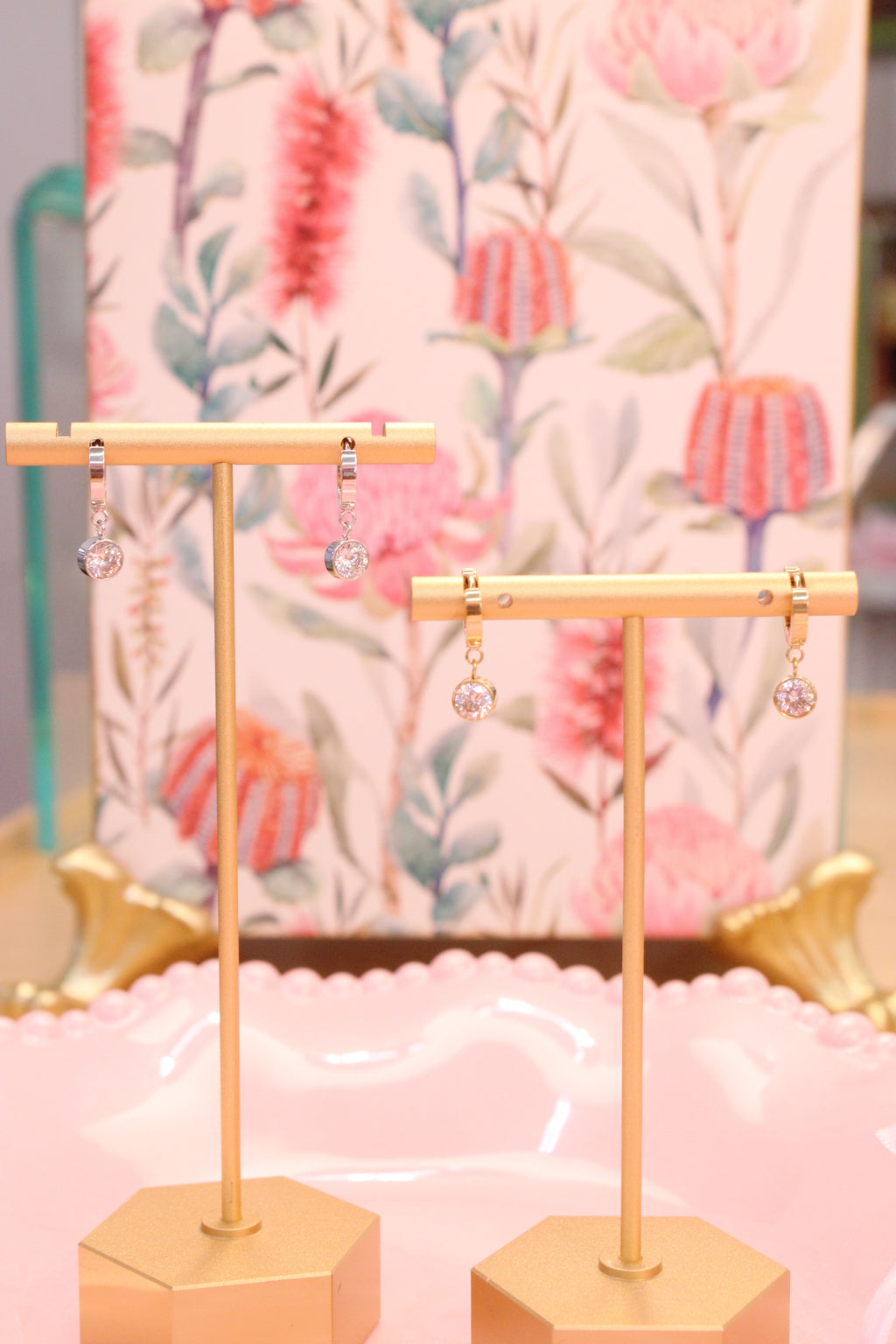 Two gold earring stands with gold and silver hoop earrings with small drop diamond against a floral background