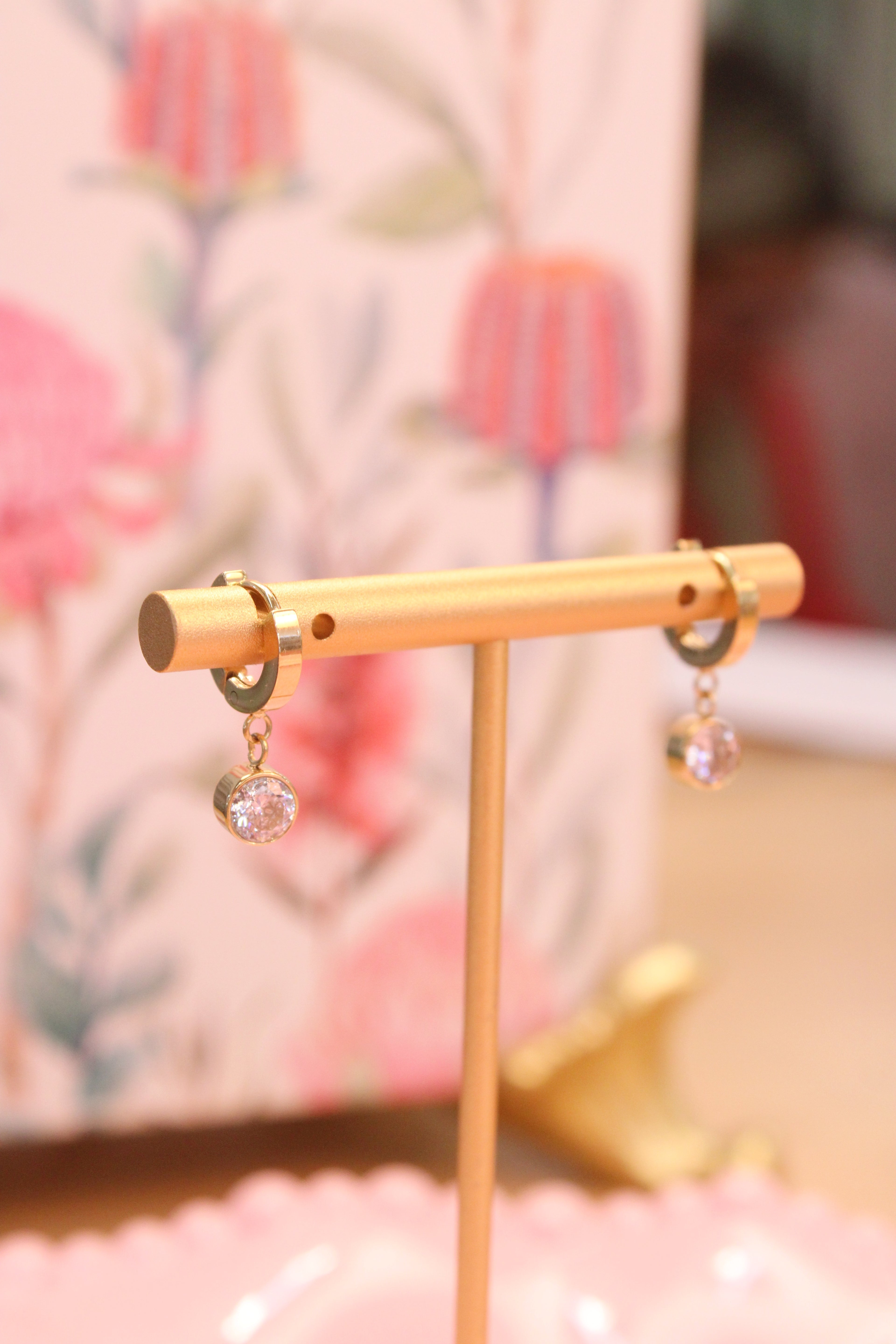 Gold earring stand with Gold hoop earrings with small drop diamond on a blurred floral background