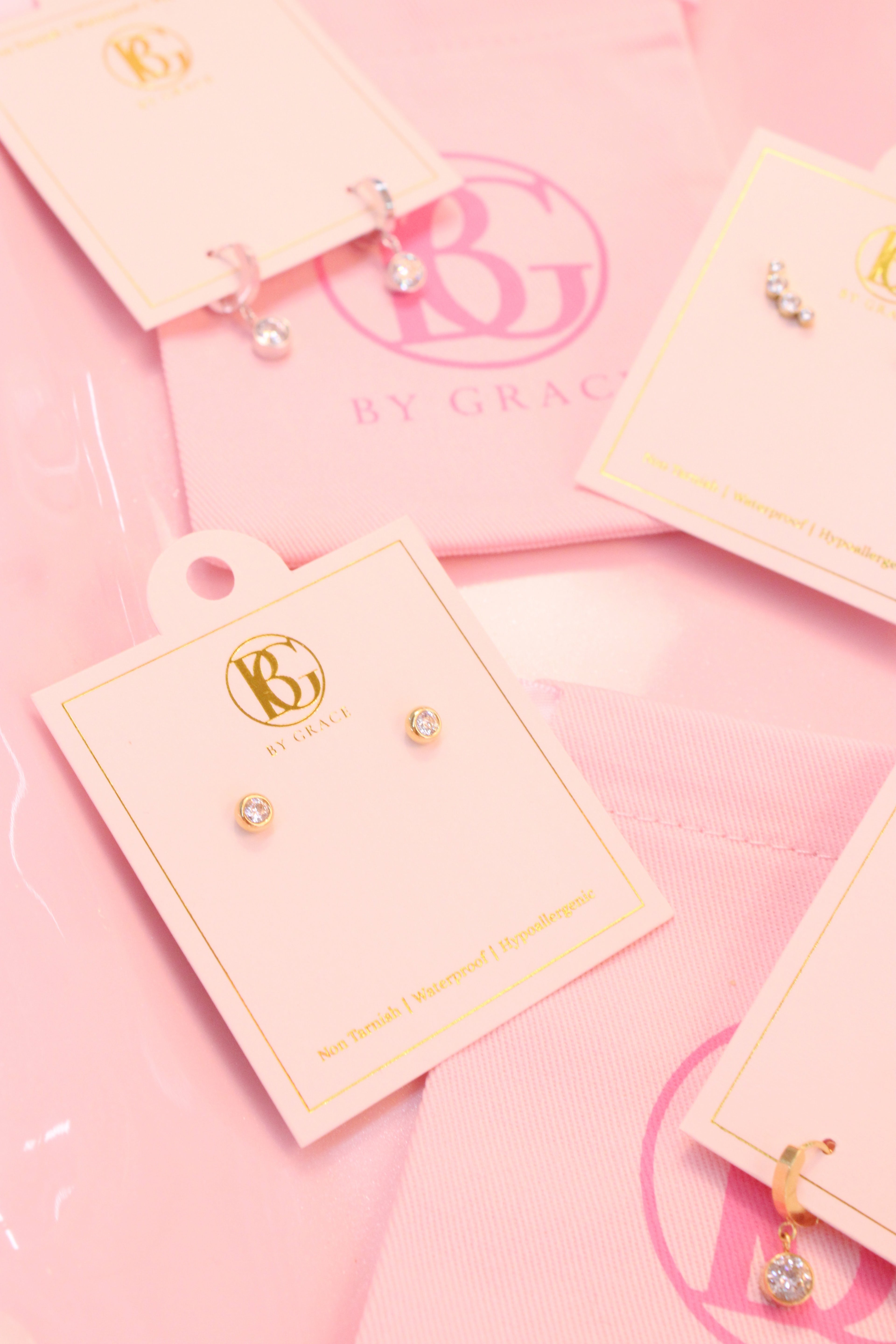 Bezeled diamond earrings on branded card with pink background