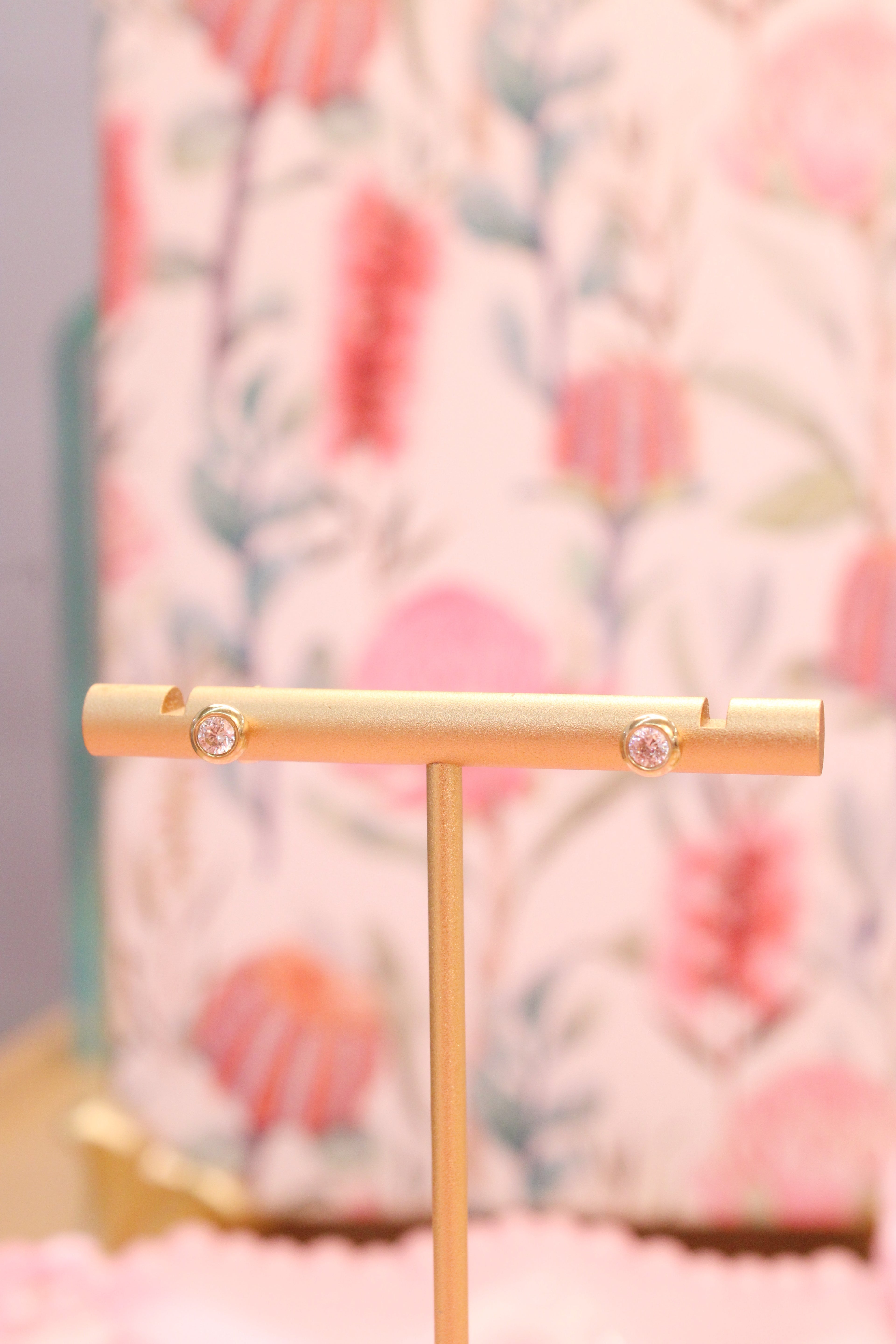 Bezeled diamond earrings on a stand  against a blurred floral background