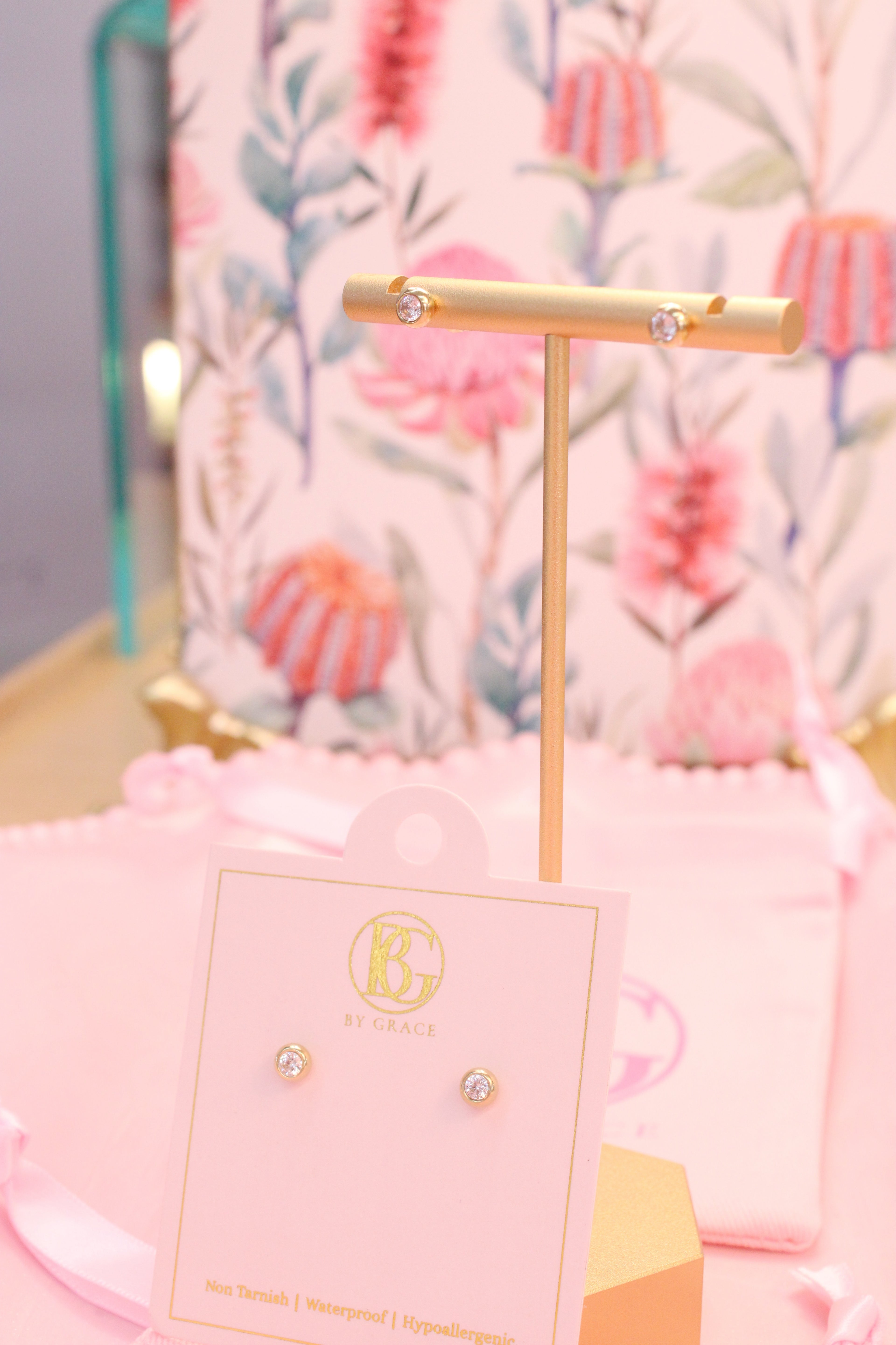 Bezeled diamond earrings on a stand with a pink card in front of a floral background
