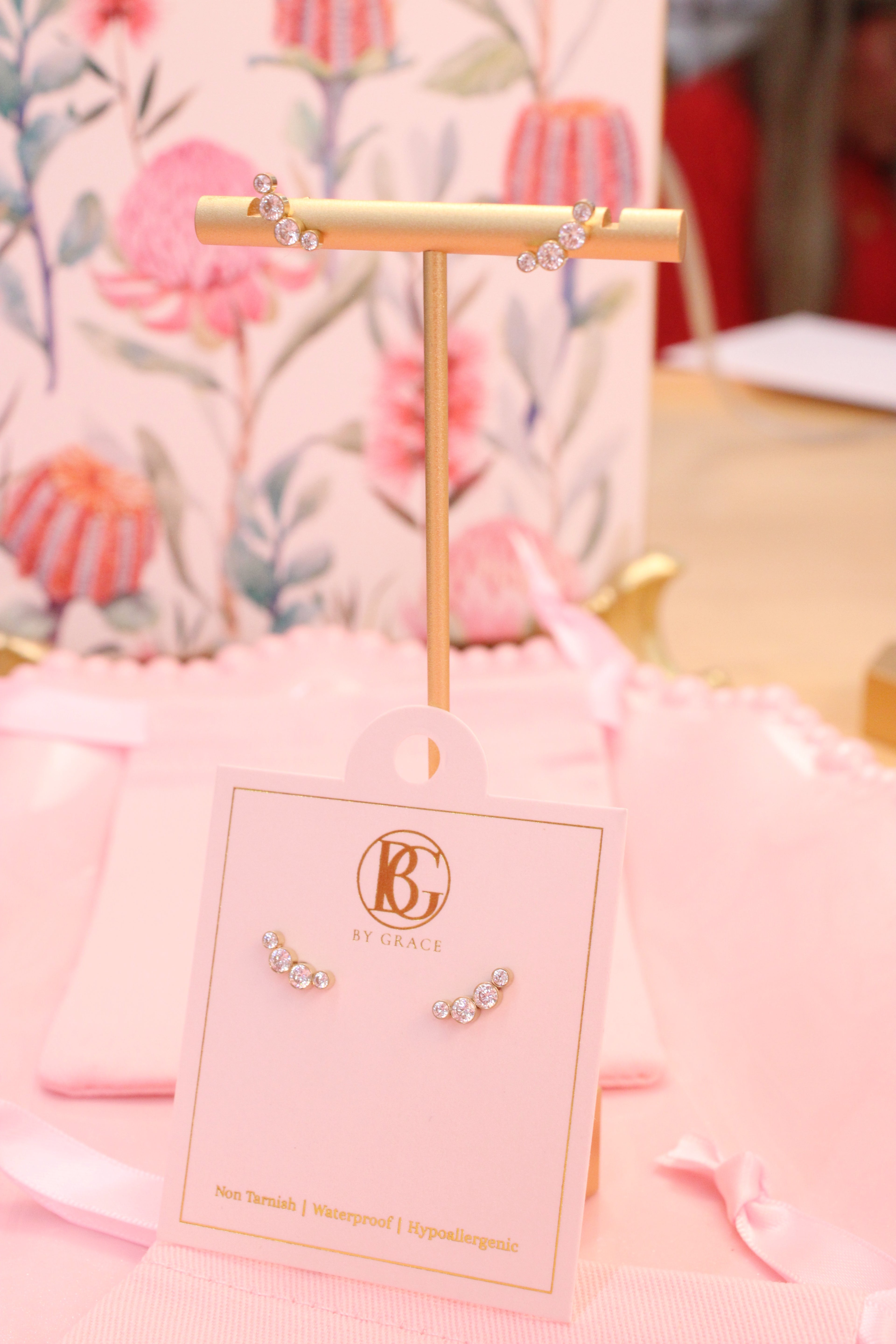 Gold earring stand with earrings on a pink card against a floral background