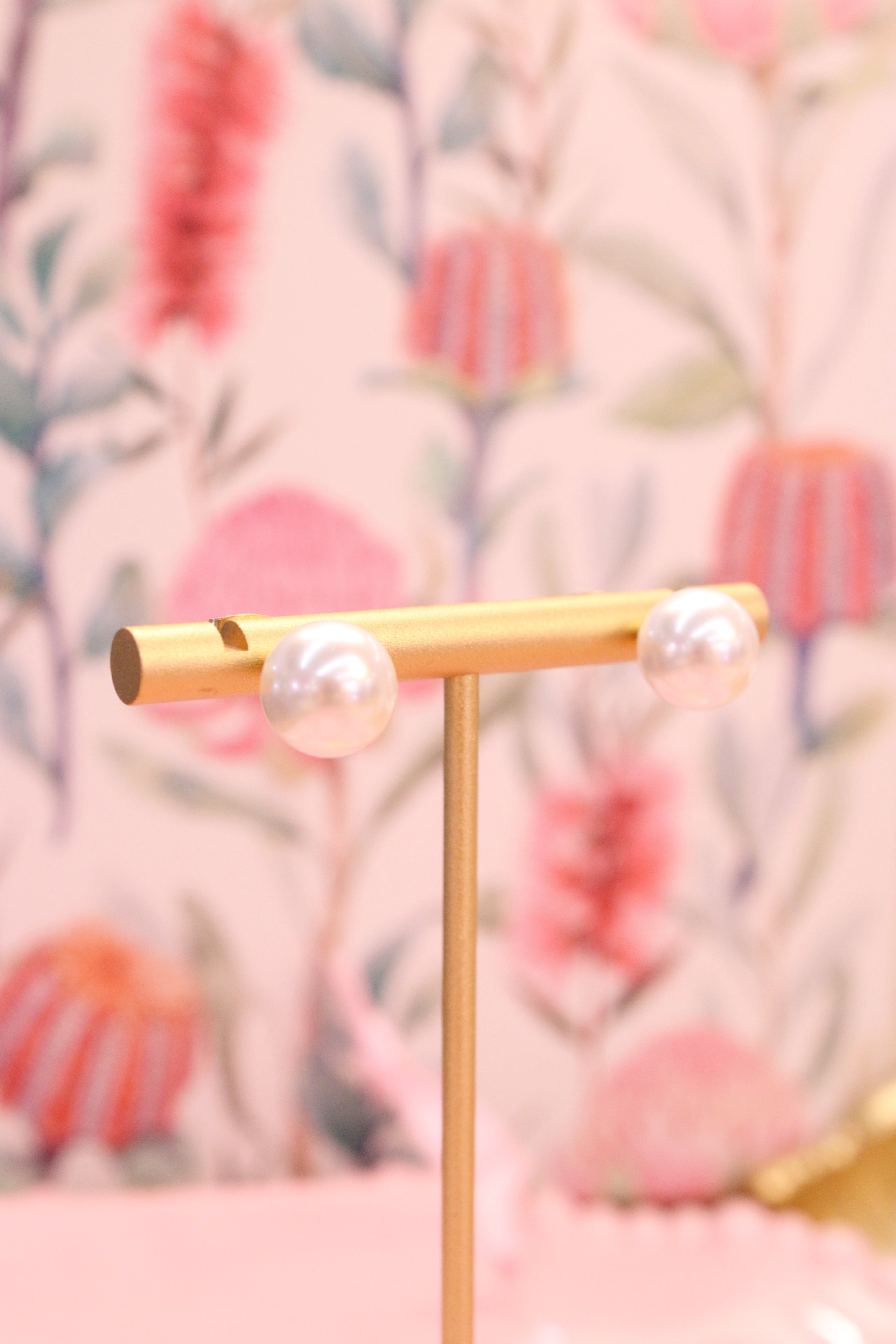 Gold earring stand with pearl earrings against a floral background