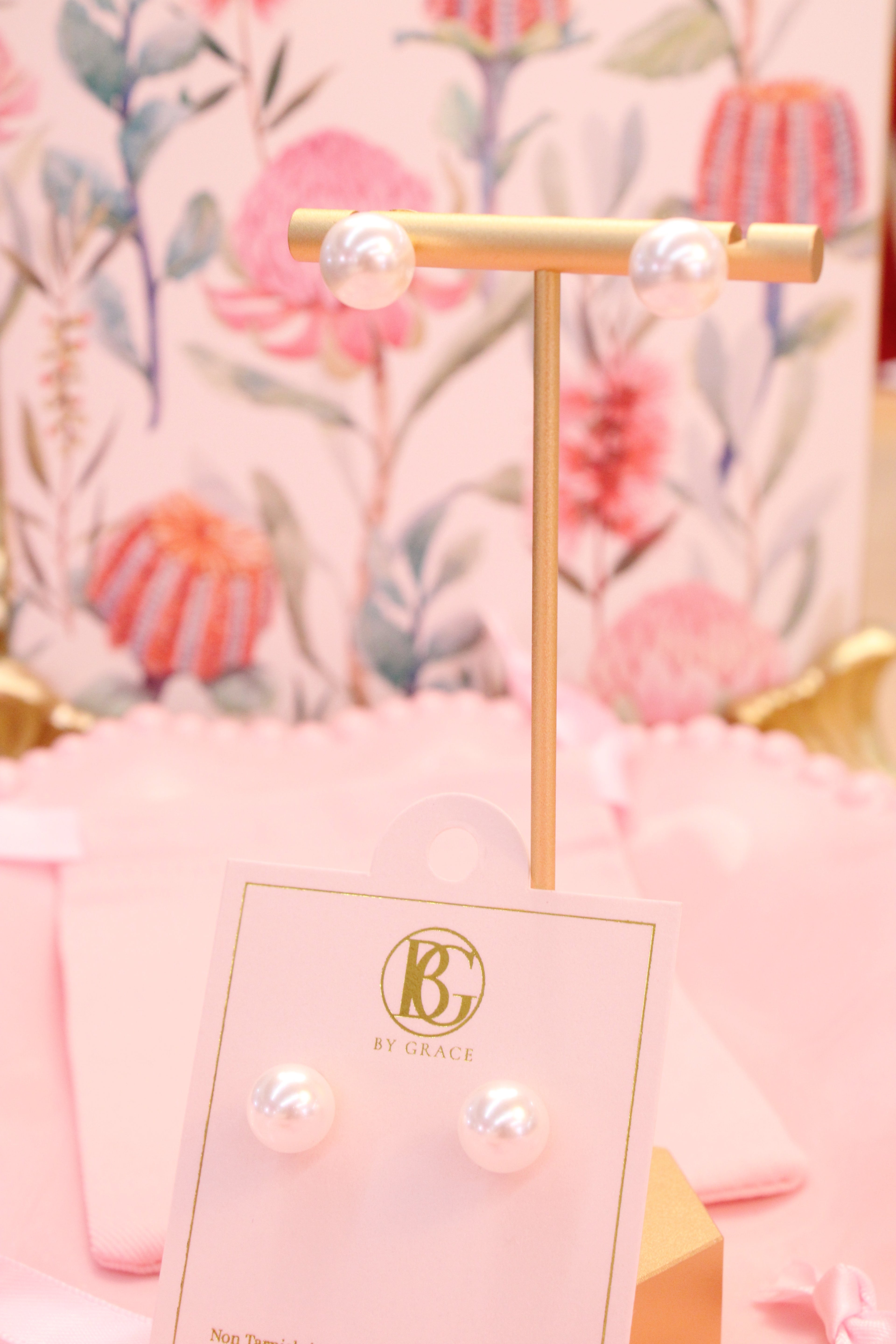 Pair of pearl earrings on a gold stand with a floral background