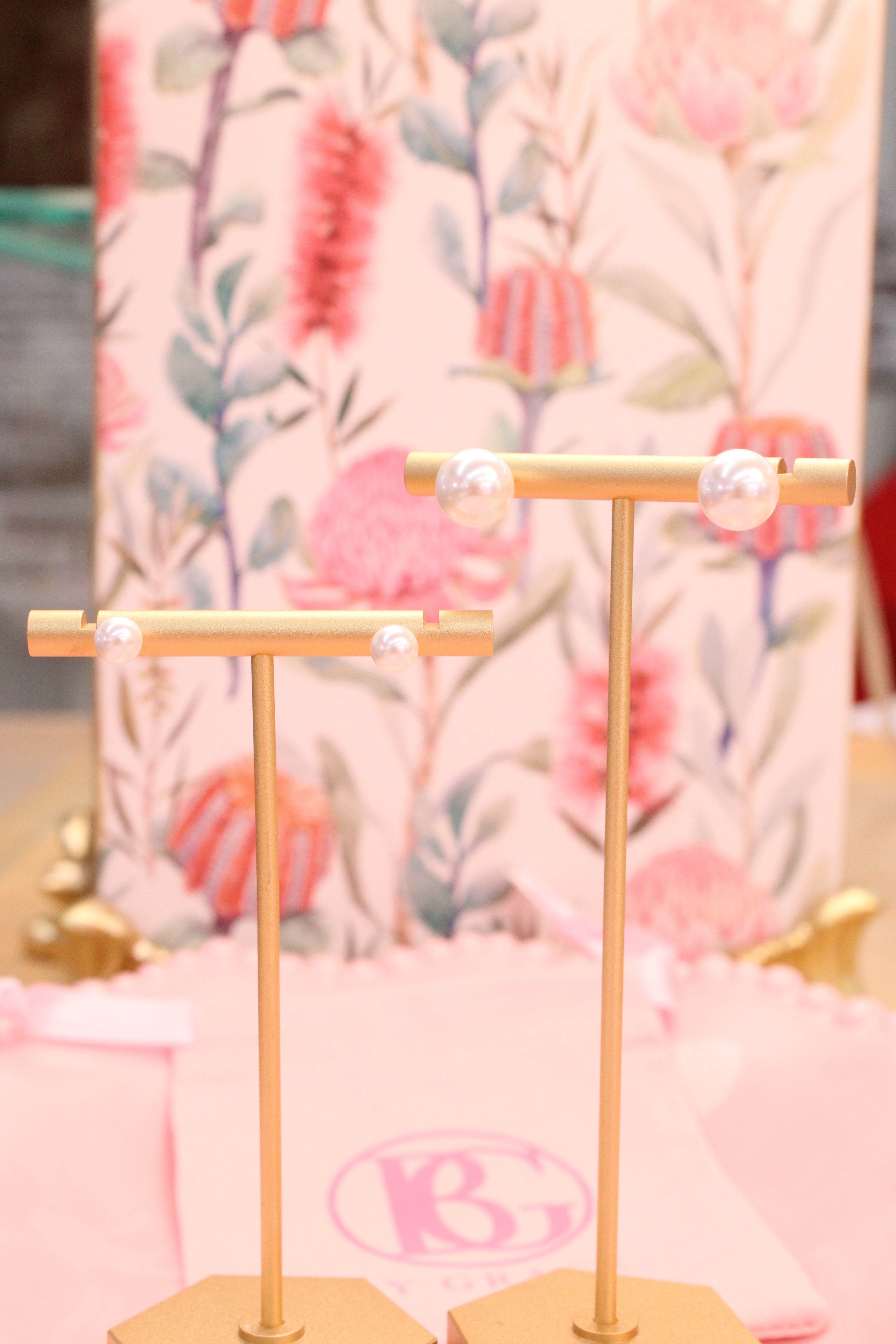 Gold jewelry stand with pearl studs with a blurred floral background