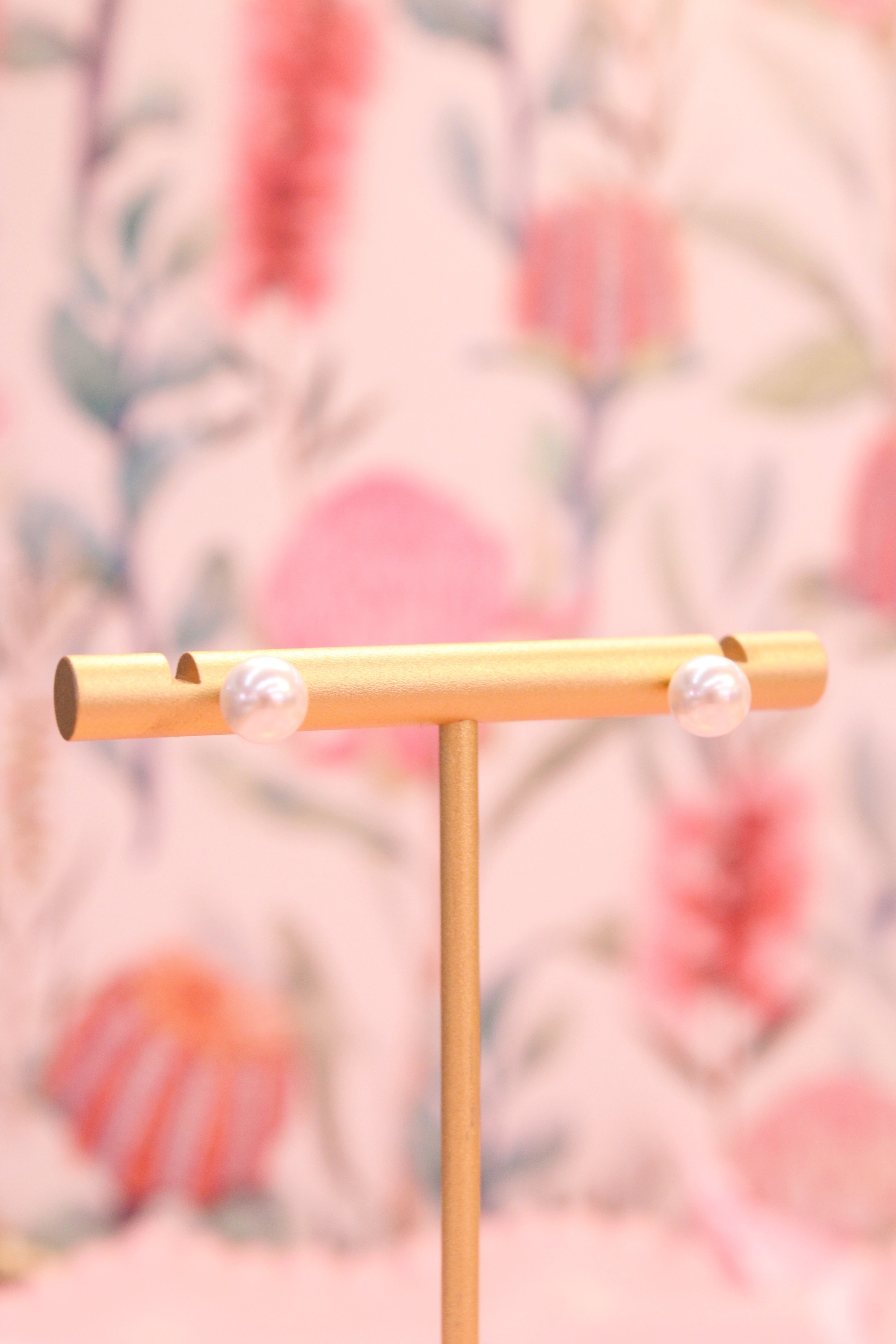Gold T-bar earring stand with pearl stud earrings on a floral background