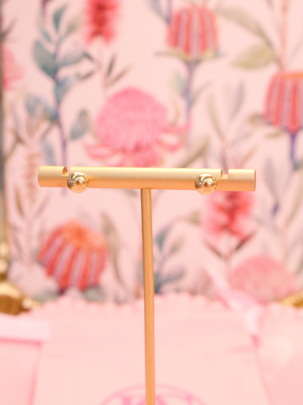 Gold T-shaped stand with gold ball earrings against a floral patterned background
