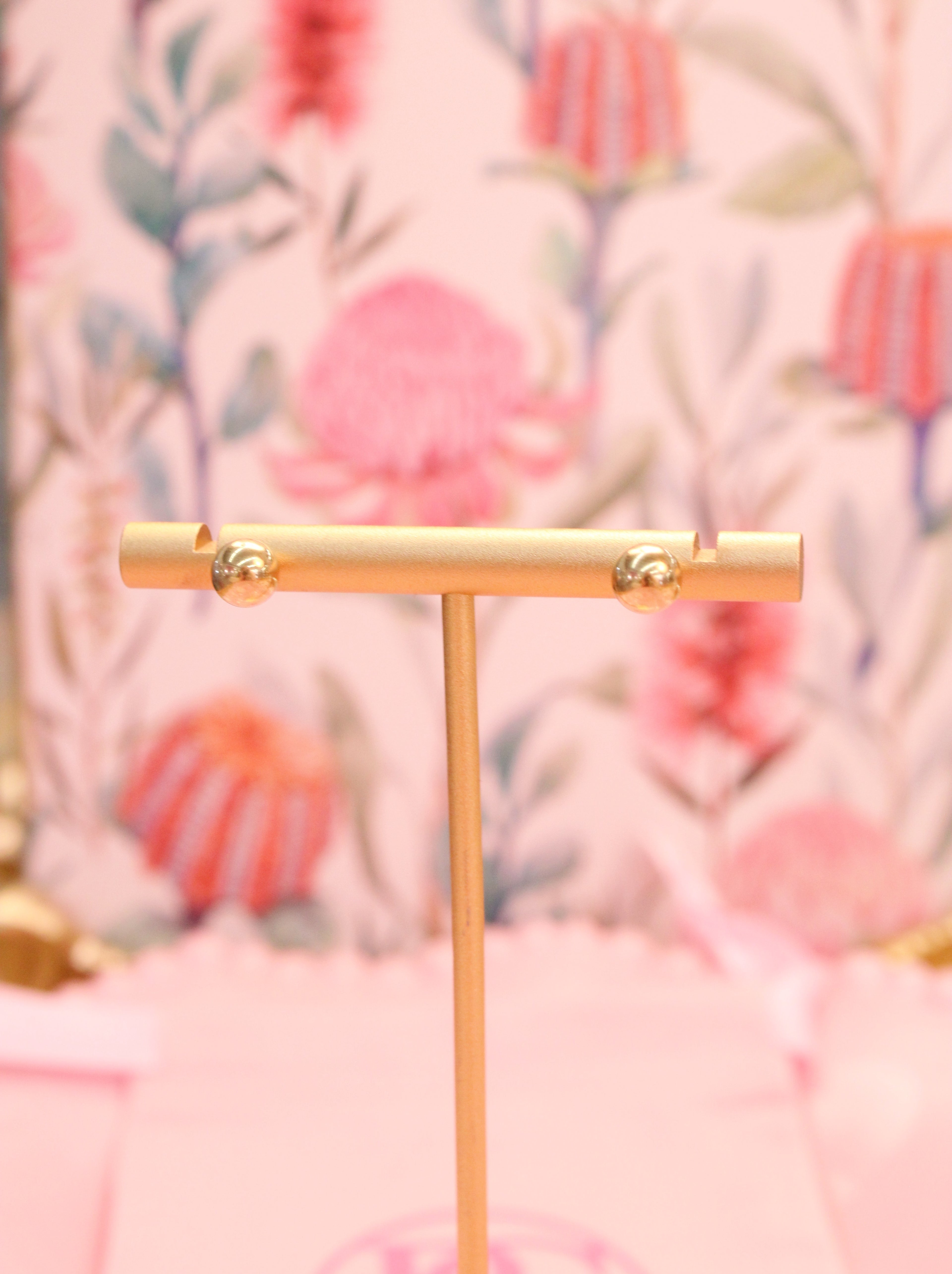 Gold T-shaped stand with gold ball earrings against a floral patterned background