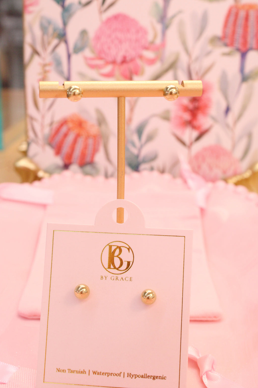 Gold cross earring on a branded card with a floral background