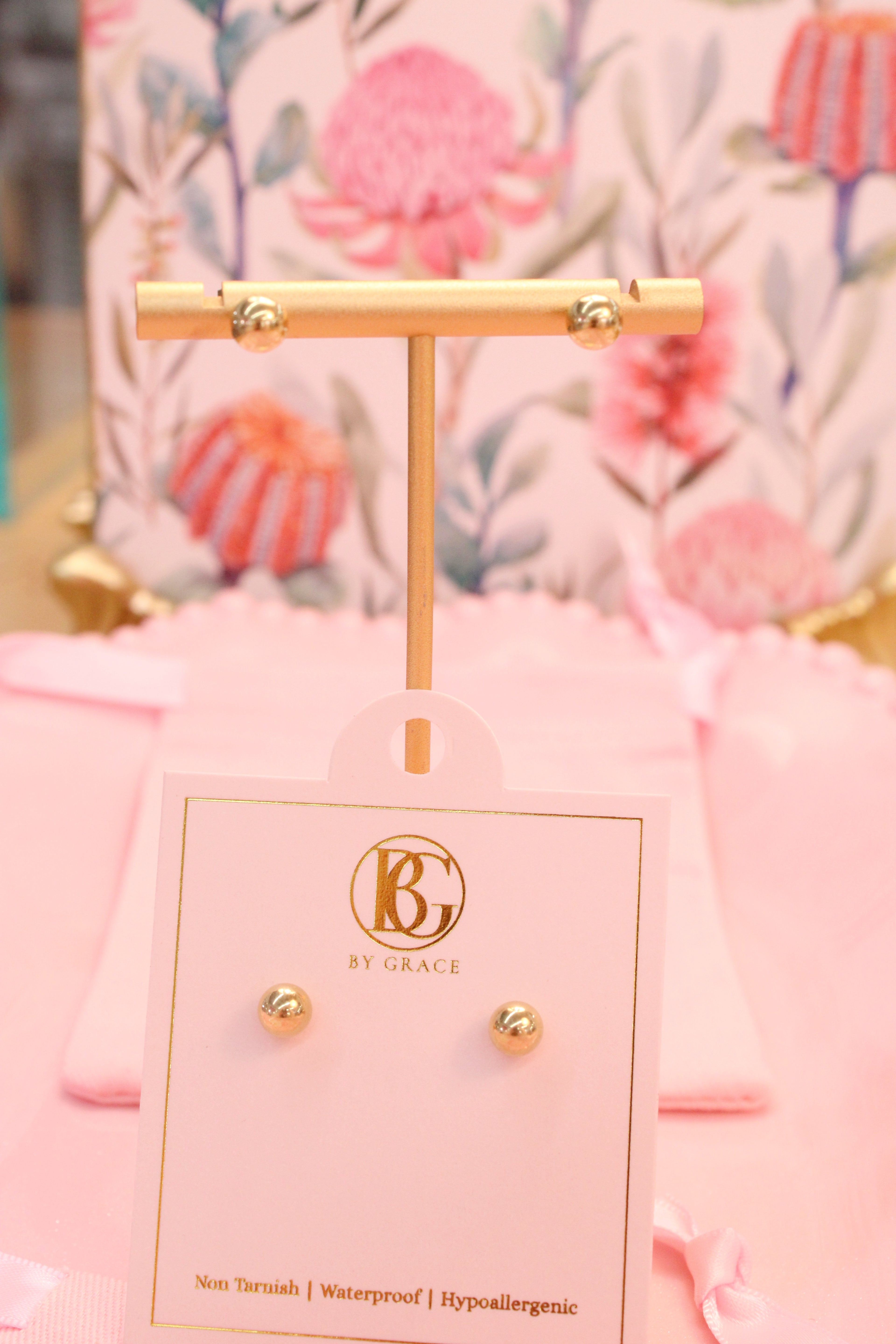 Gold cross earring on a branded card with a floral background