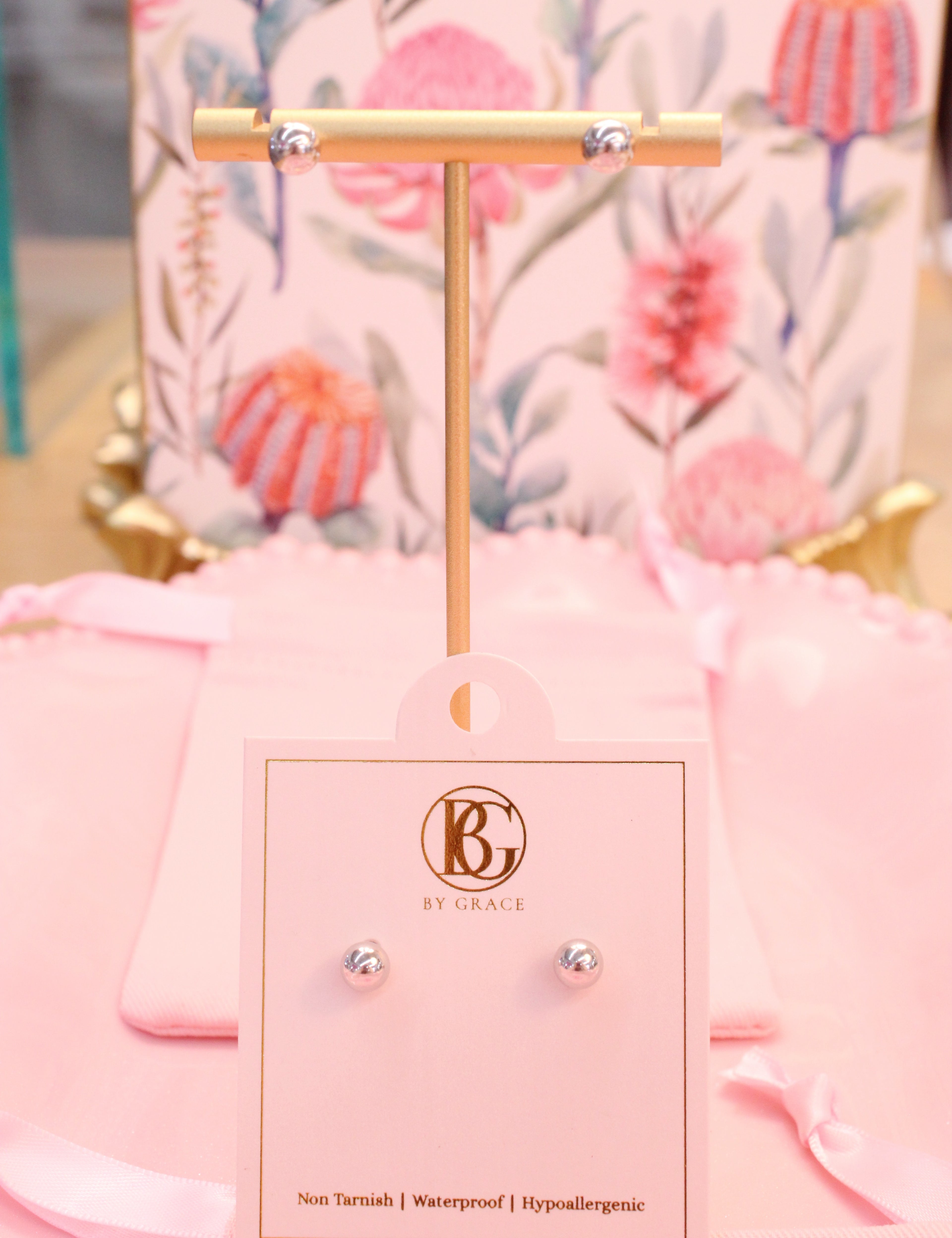 Pair of silver ball earrings on a pink card with 'By Grace' branding against a floral background