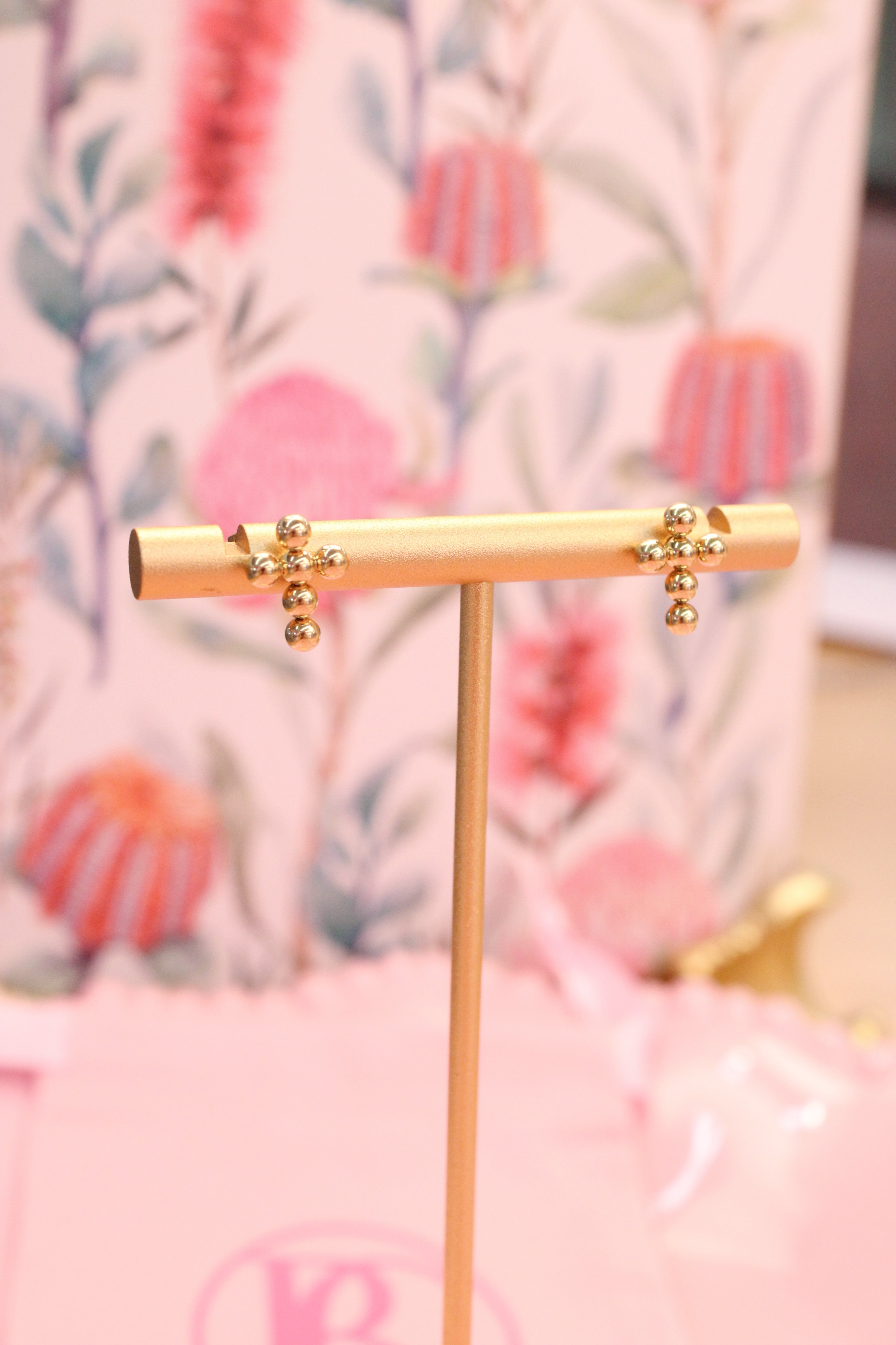 Gold earring stand with cross earrings on a floral background