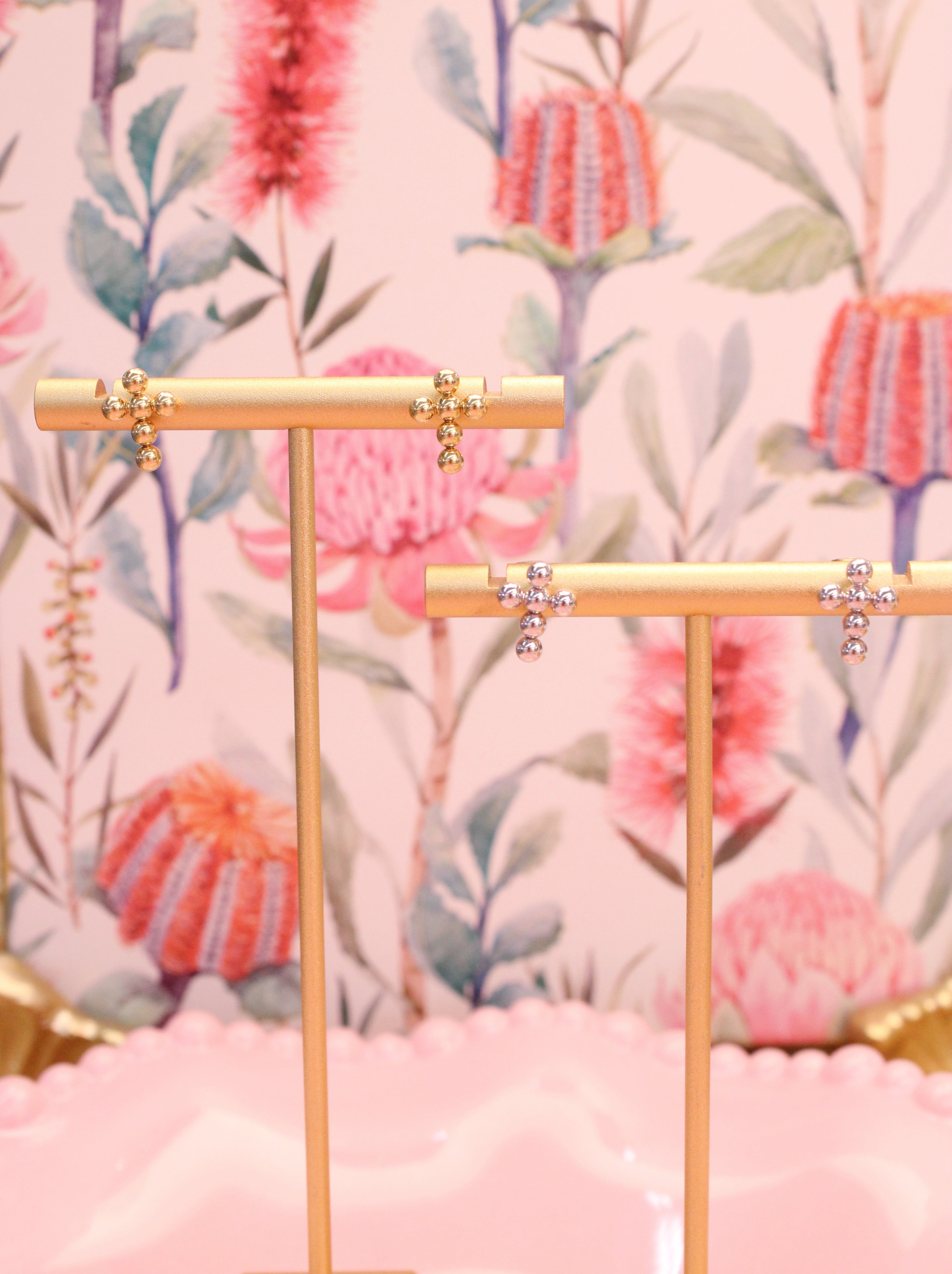 Gold bar with cross earrings and decorative elements on a floral patterned background