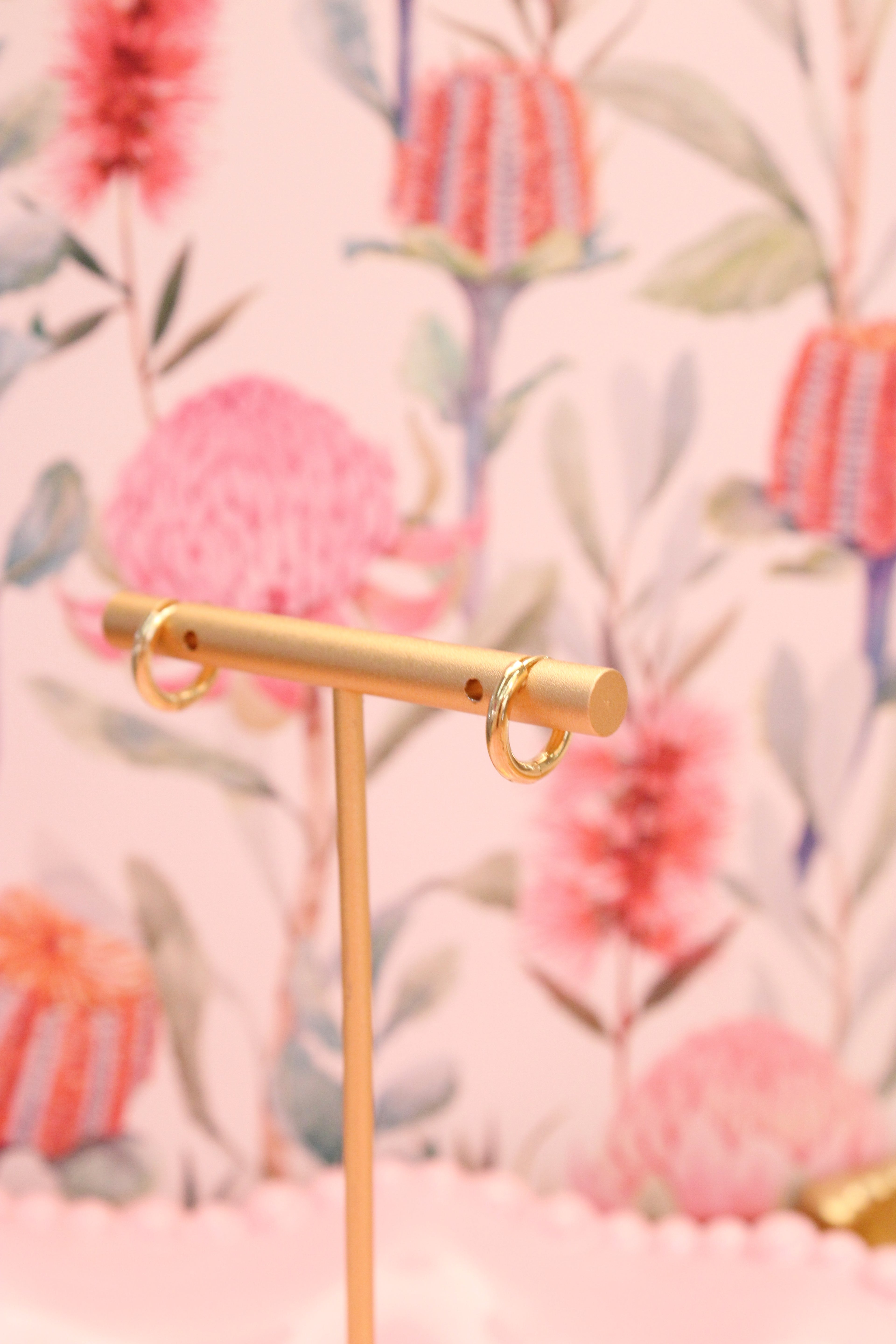 Gold earring stand with gold hoops against a floral background