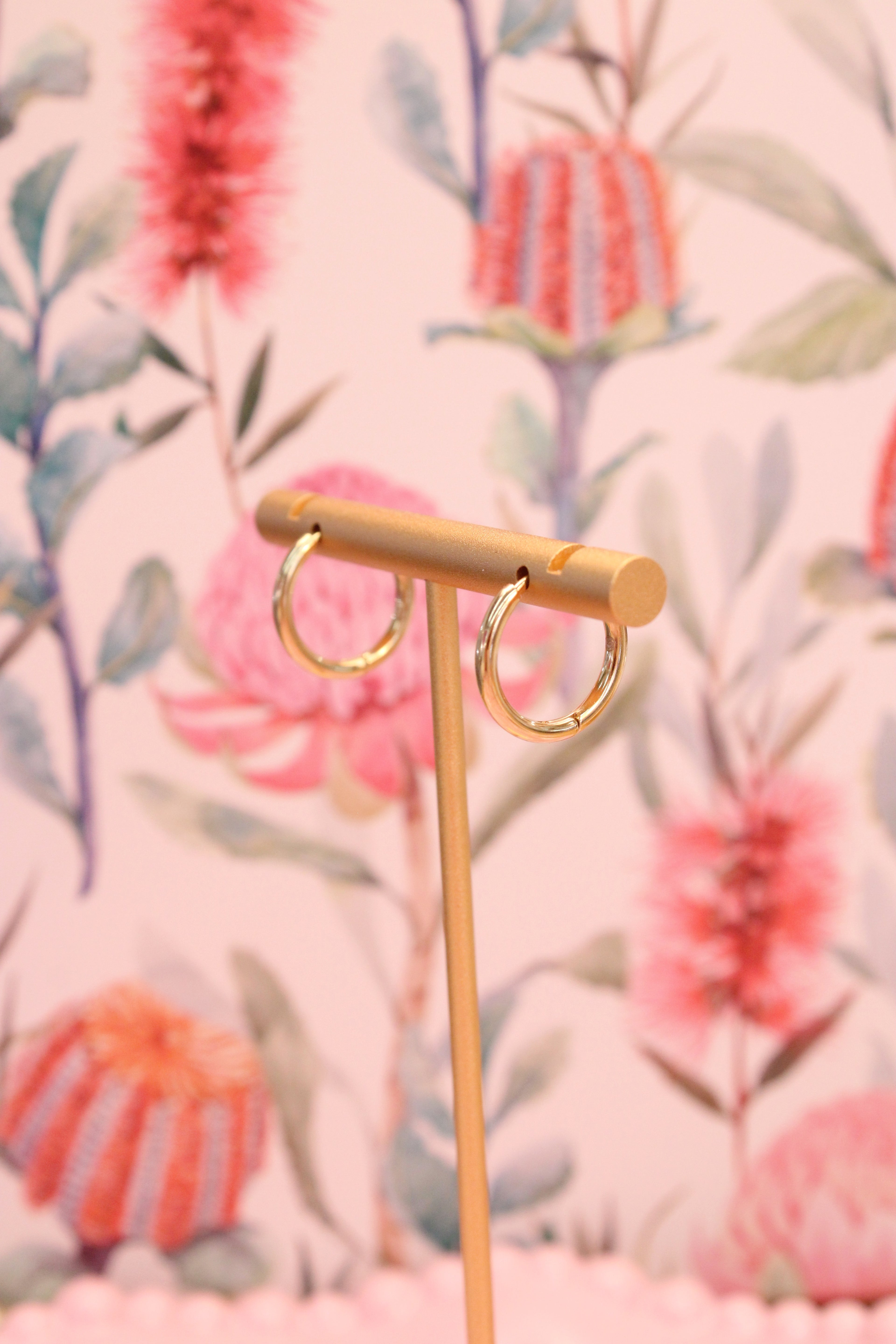 Gold earring stand with gold hoops on a floral background
