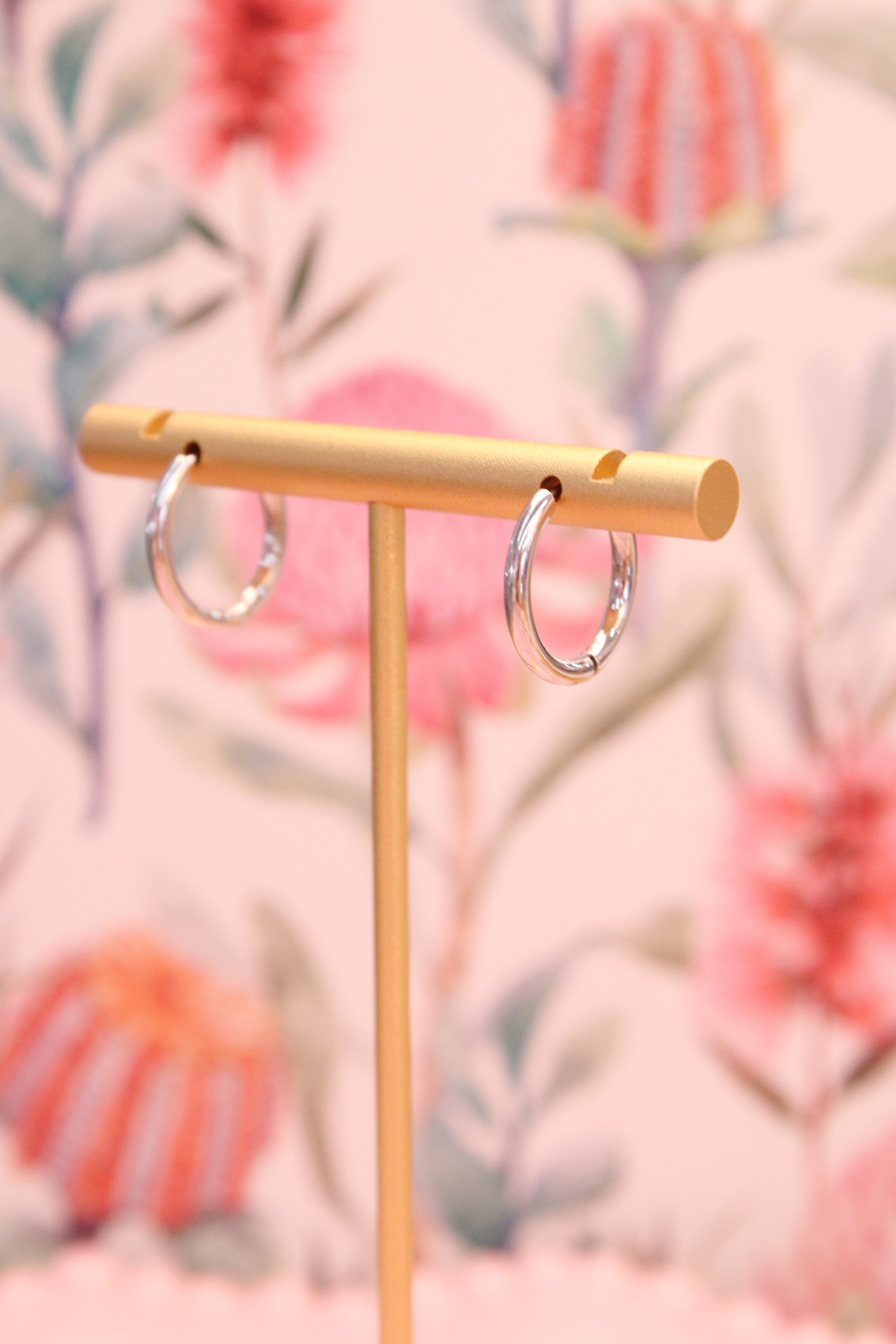 Gold earring stand with two silver hoop earrings against a floral background