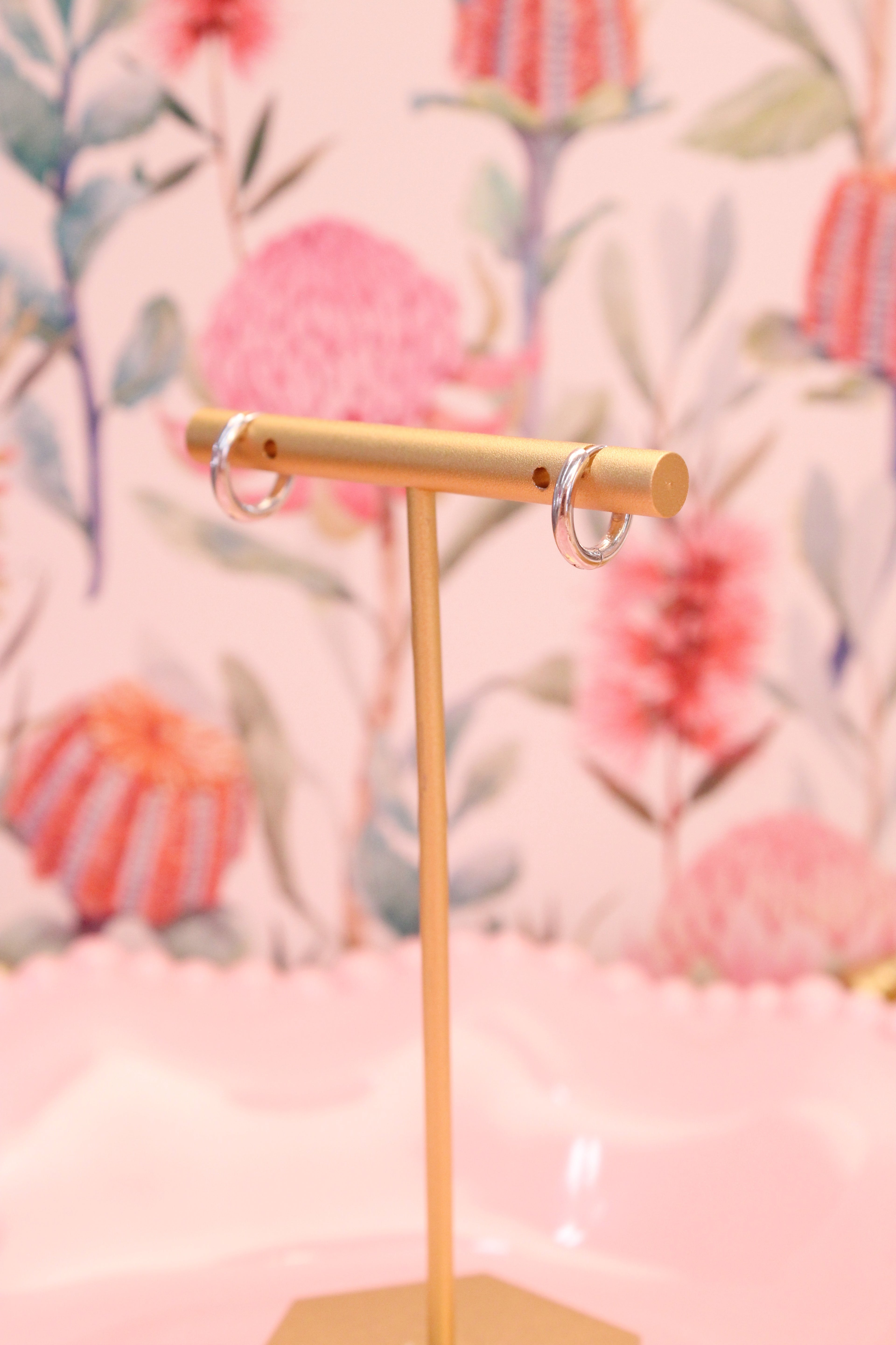 Gold earring stand with silver hoops against a floral background